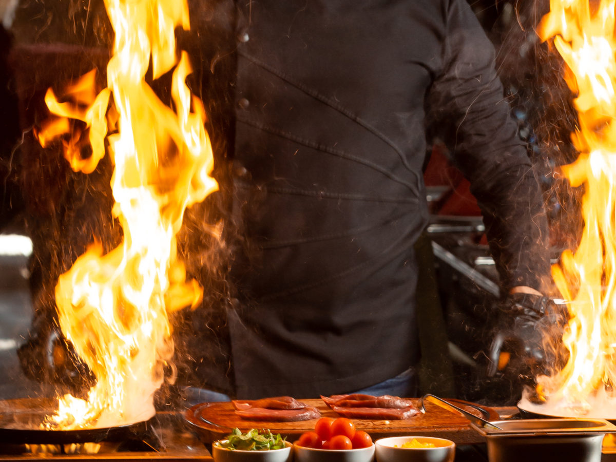 chef holds two frying pans with burning fire