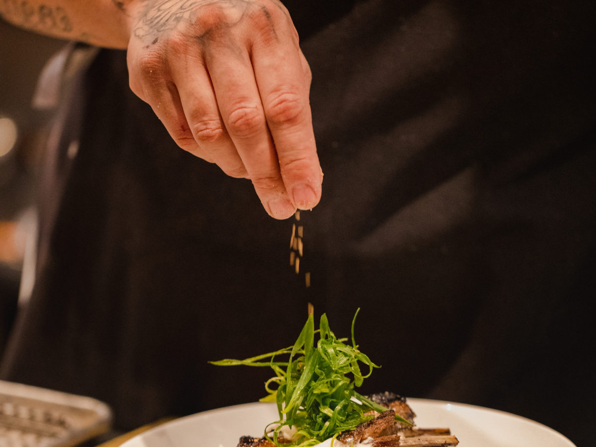 chef pouring seasoning on beef stake on plate